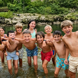 Grupo de niños sonriendo y bañándose en un río en plena naturaleza durante el campamento de verano de InterWay